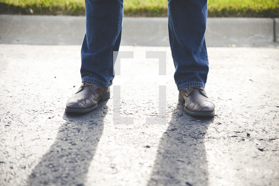 A man's legs standing on a sidewalk.