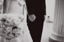 A bride and groom stand with hands held