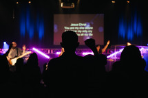 silhouettes of parishioners standing with raised hands at a worship service 