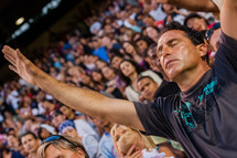 Man with eyes closed and face towards the sky with both arms raised in audience of people during worship service.