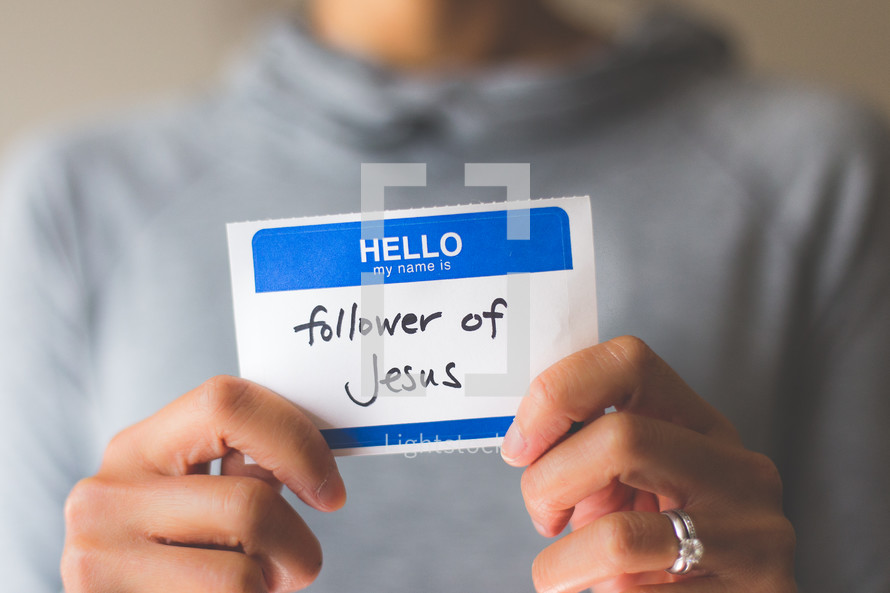 woman holding a name tag with the words follower of Jesus 