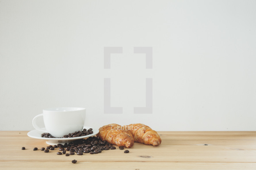 coffee beans, cup and saucer, and croissants on wood countertop 