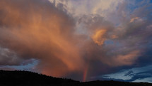 rainbow and pink clouds in the sky at sunset over mountains 