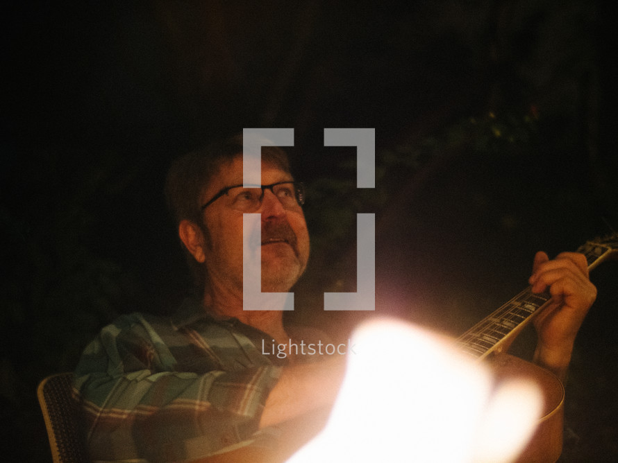 a man playing a guitar by a campfire 