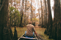 man on a canoe paddling through a swamp 