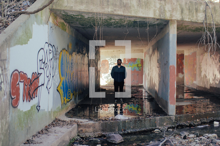 a man standing under concrete tunnels covered in graffiti 