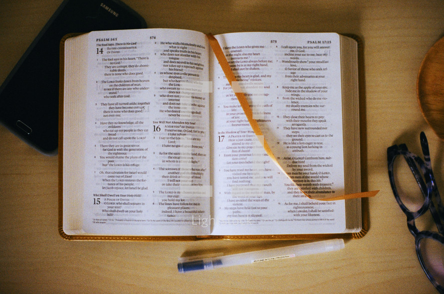 A bible, glasses,  phone, and pen laid out for reading. 