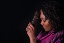 African American woman holding a Bible to her head 