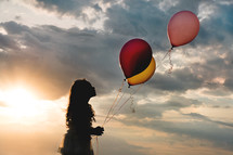 a girl child holding balloons at sunset 