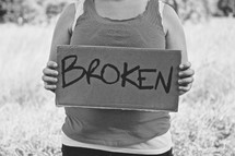 woman holding a sign with the words BROKEN