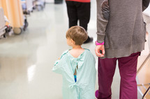a boy child in a hospital gown walking with a nurse 