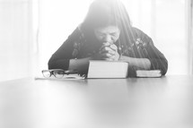 a woman sitting praying over a Bible 