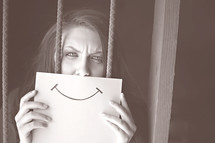 woman hiding behind a smiley face picture, behind bars