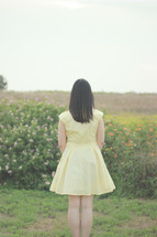 a young woman in a yellow dress standing with her back to the camera 