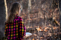 a girl walking outdoors reading a Bible 