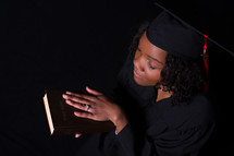 female graduate holding a Bible and praying 