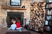 children sitting in front of a fire in a fireplace 