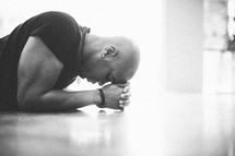 Man with head on hands praying on the floor.