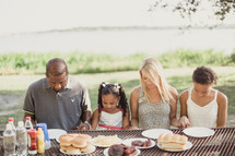 family holding hands in prayer at a picnic table 