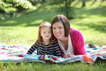 Mother and daughter laying on a blanket in the grass outside