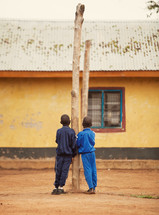 two young boys leaning on a tree trunk