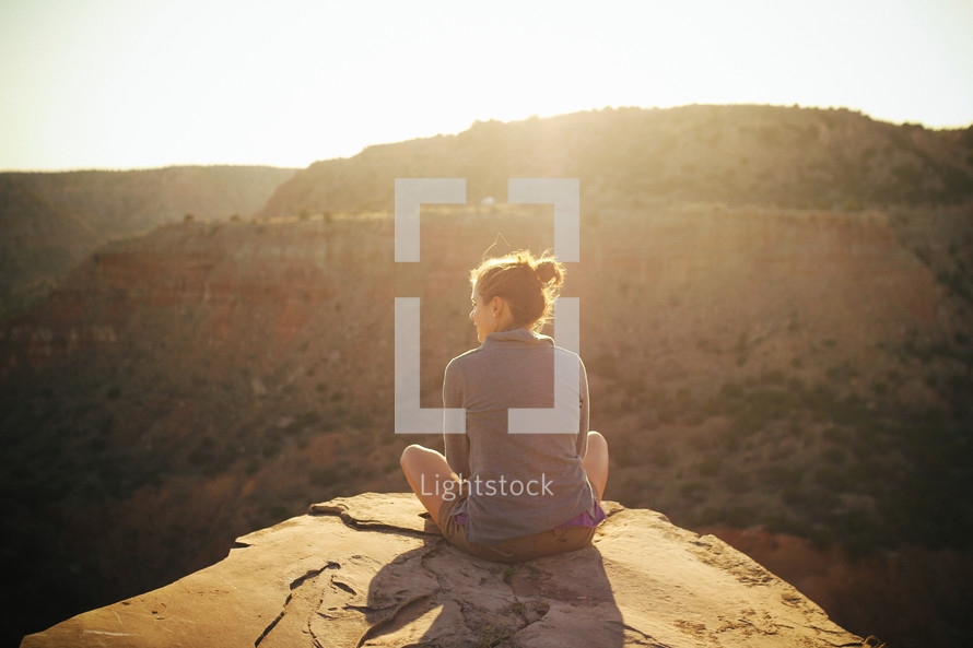 a woman sitting outdoors at the top of a canyon at sunset 