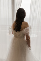 Back view of a bride looking out a window on her wedding day.