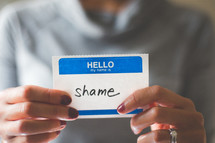 woman holding a name tag with the word shame 