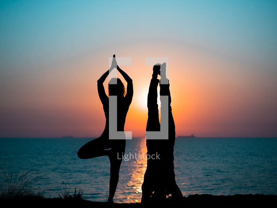  Silhouette of young woman and man doing pair yoga on sea beach at sunset. Meditation. Couple practicing acro yoga. Flexibility workout at nature background.
