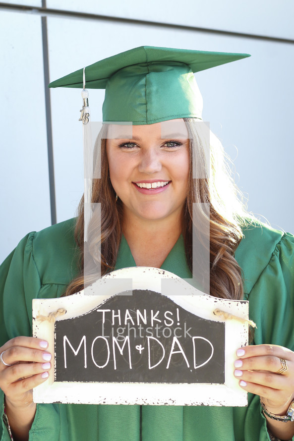 a graduate holding a thanks mom and dad sign 