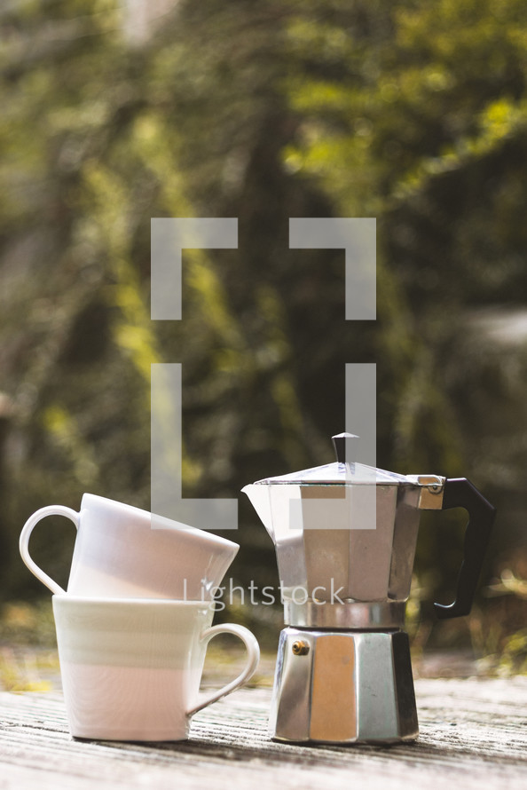 coffee pot and stacked mugs outdoors 