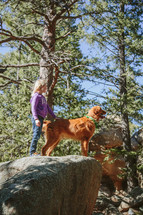 a little standing with her dog on a rock in a forest 