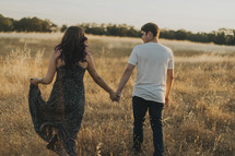 a couple holding hands walking through a field of tall grasses