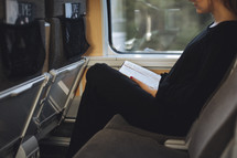 A girl sitting on a train a train reading her bible. 