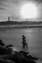 man with a bicycle on a beach and a distant lighthouse