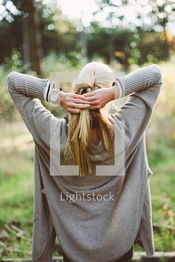 a woman braiding her blonde hair outdoors 