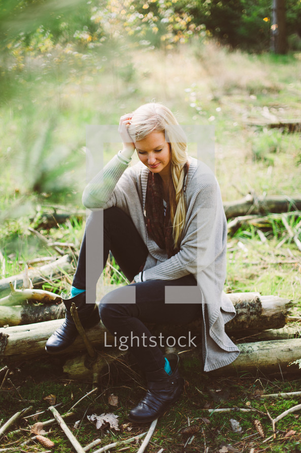 blonde woman sitting on a fallen tree 