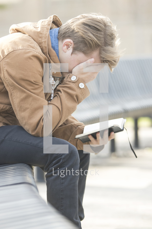 a man covering his face in shame while reading a Bible 