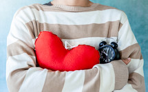person Hugging a red heart and alarm clock, valentine day background.