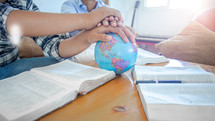 hands on a globe at a small group Bible study 