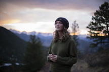 a woman in a wool cap standing on a mountaintop at sunrise 