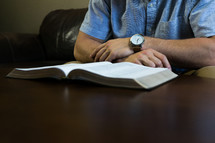 a man sitting on a couch reading a Bible on a coffee table 