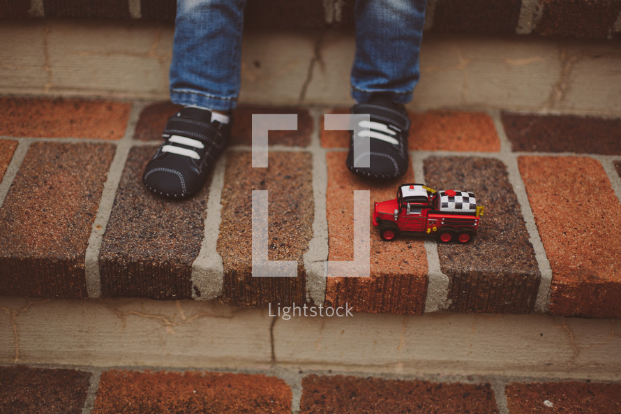 toddlers feet and a toy firetruck on steps