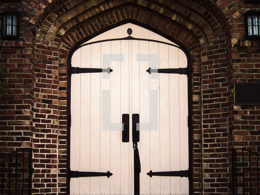 Large white wooden doors in an arched brick entryway.