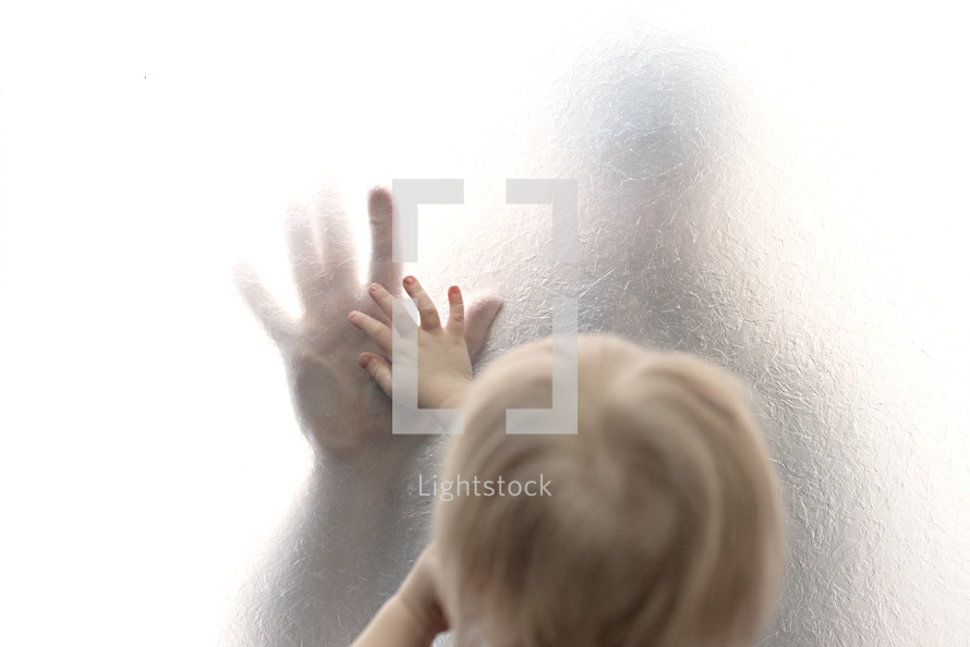 child touching parent's hand through frosted glass 