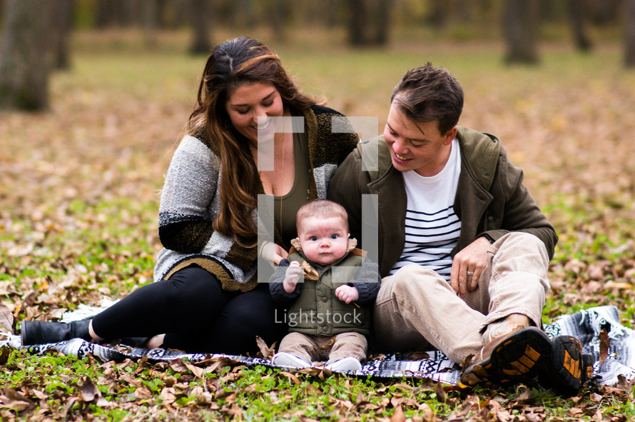 portrait of a young family sitting on a blanket in the grass 