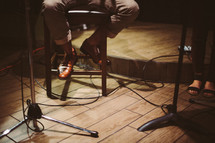man sitting on a stool and microphone stands 