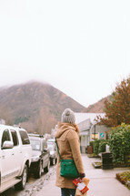 A woman in winter clothes stands on a sidewalk in a mountain town.