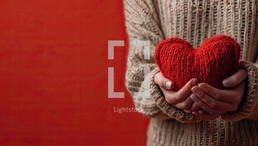 Female hands holding a red heart on a red background with copy space