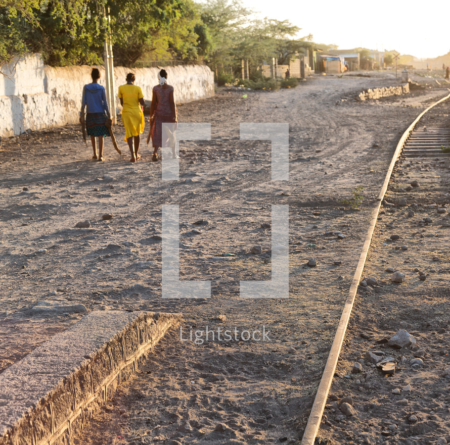 women walking on a dirt road next to tracks in Africa 